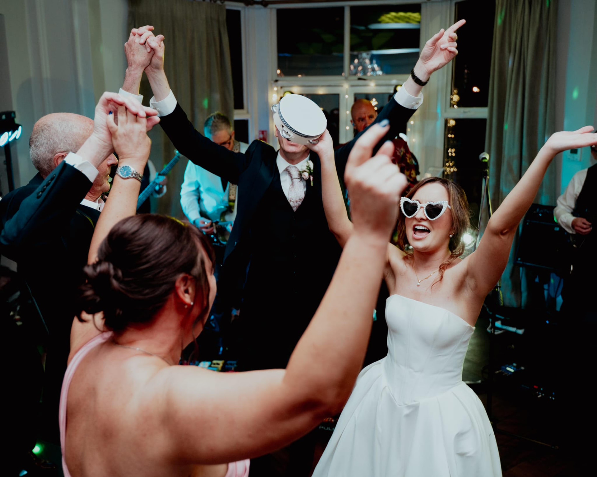 Bride and guests dancing with arms raised on a packed dance floor
