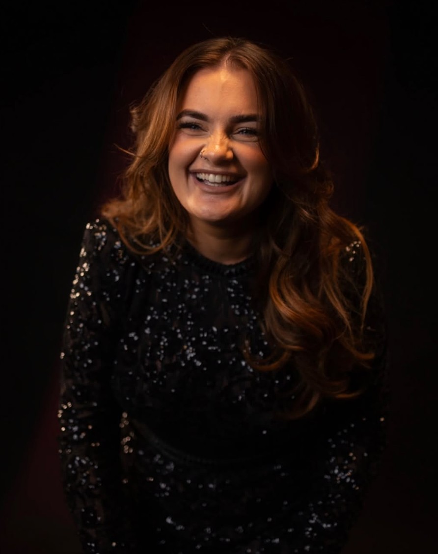 A live vocalist in a sparkling black sequined dress, laughing against a dark background