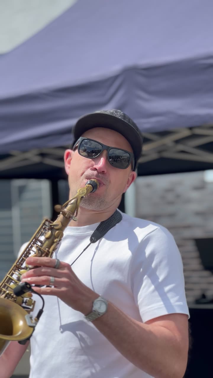 A saxophonist playing outdoors at a daytime celebration