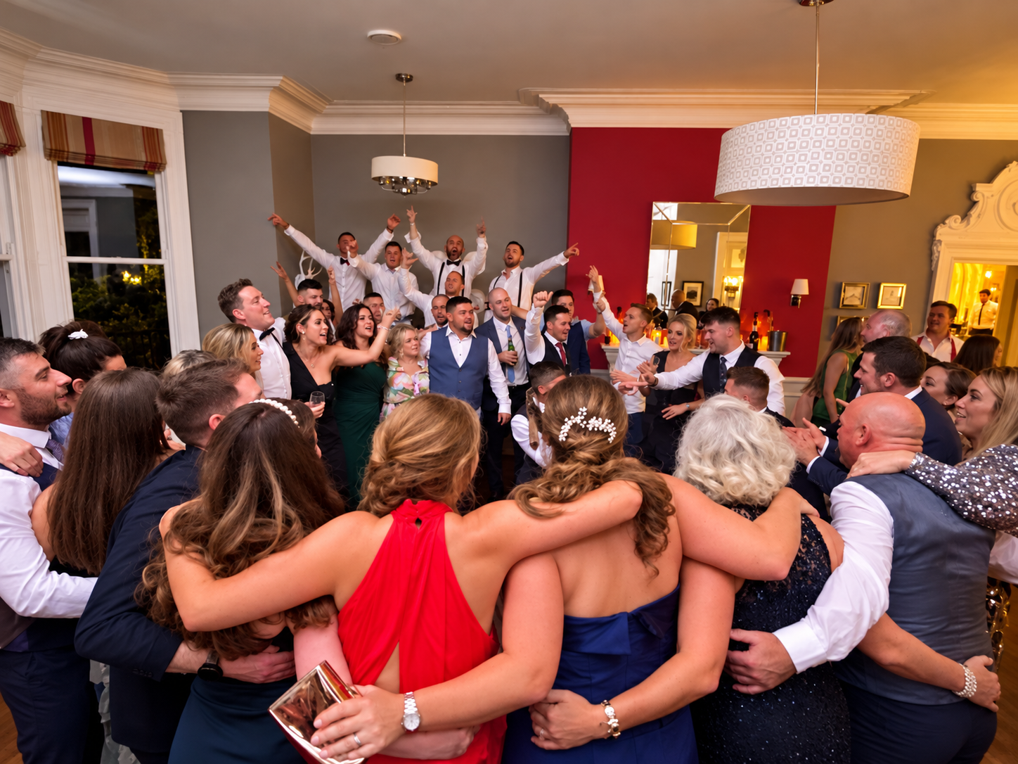 Wedding guests arm in arm in a circle while the groomsmen cheer on the dancefloor