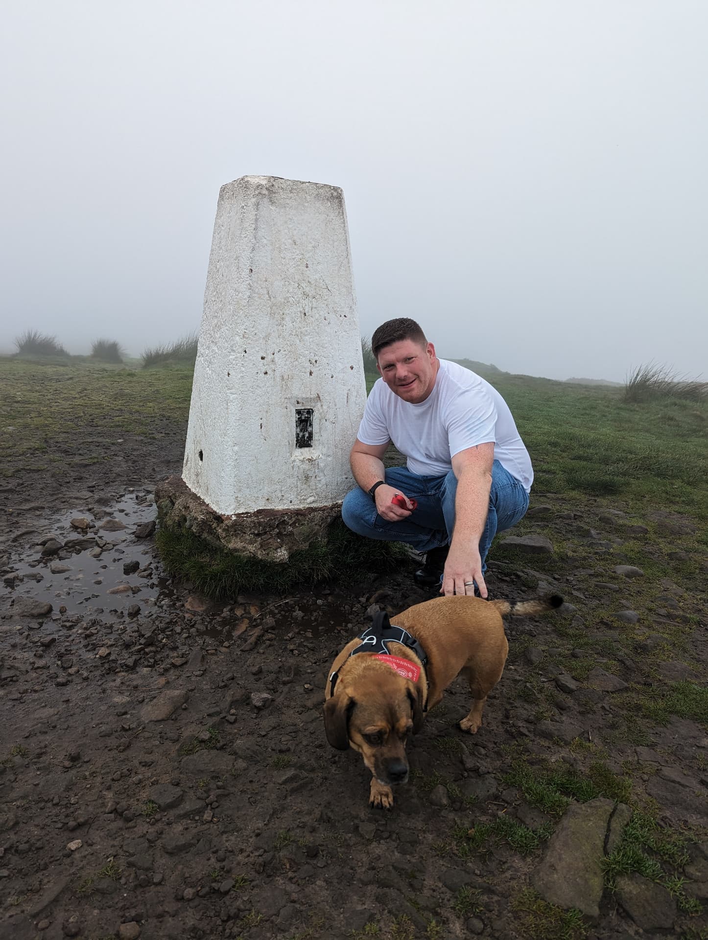 Jon crouching beside his dog Rio on a misty hilltop walk