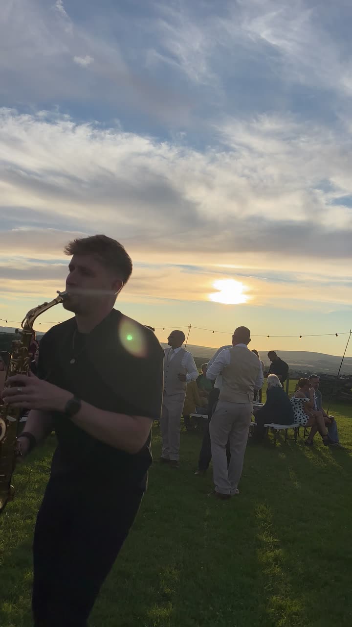 Guests dancing on the lawn alongside a saxophonist at sunset