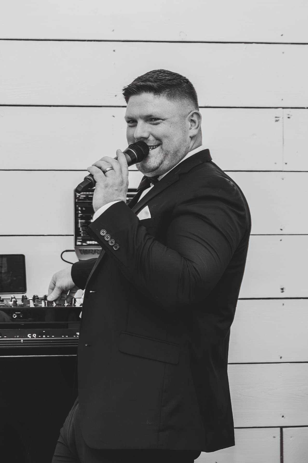 Jon in a tuxedo with a microphone at the DJ decks