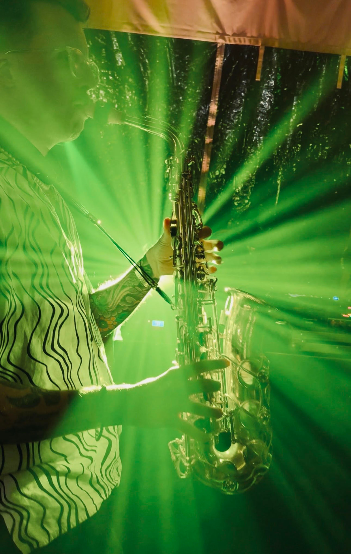 A live saxophonist performing under green stage lights