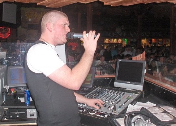 Jon on the microphone behind a club DJ booth